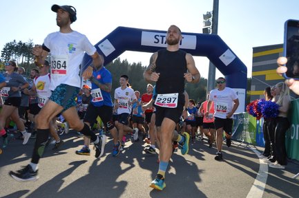 Firmenläufer rennen von einem aufblasbaren Tor mit der Aufschrift "Start" in Richtung der Kamera